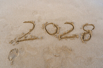 2028 numbers written on sandy beach. Sea background.