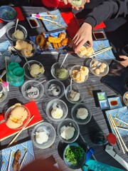 Table with ice cream bowls, fried snacks, hands and chopsticks