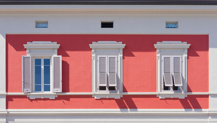 Old neoclassical italian facade with window and wooden shutter against a red colored plaster wall