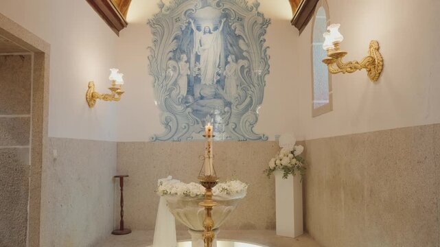 baptismal font with paschal candle and floral decor under blue azulejo mural in church