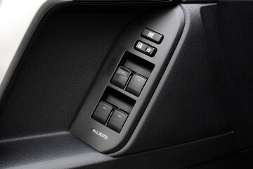 Close-up of black car door panel with power window control buttons, lock switches and textured surface, showing modern automotive interior design and functionality.