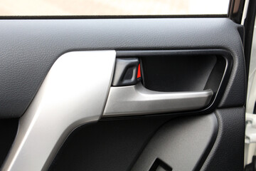 Close-up of a car interior door handle in silver metallic with black textured plastic and a small...