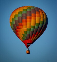 Naklejka premium A colorful hot air balloon floats in a clear blue sky. The balloon features a vibrant pattern of orange, green, and yellow panels. It is a serene scene of flight.
