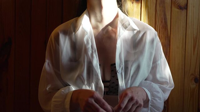 Woman undressing white shirt, revealing black bra in sunlit wooden room