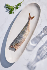 Fish on a white plate, on a marble background with transparent glasses and parsley