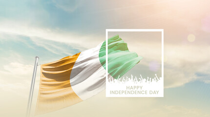 Ivory Coast flag waving proudly under a bright sky with text happy independence day. Ivory Coast...