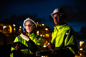 Team of construction engineers in uniforms and helmets examine project with tablet Industrial plant...
