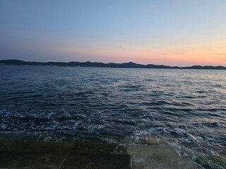 Dusk seascape with gentle waves and pastel sky over distant hills