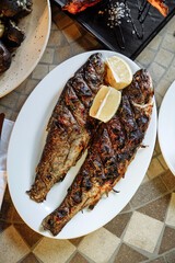 Grilled fish with lemon slices on a white plate