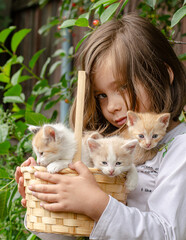 Cute five-year-old girl happily holding a basket full of fluffy kittens. Joy, childhood innocence, and love for animals concept. © tinkerfrost