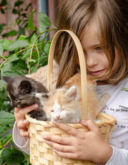 A sweet little girl smiling as she carefully holds a wicker basket with adorable kittens inside. Friendship and care. © tinkerfrost