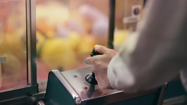 A person is playing a crane game at a carnival moving the joystick. The game is a claw machine, and the person is trying to grab a stuffed animal