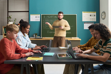 Caucasian man teaching diverse group of teenagers using laptops in classroom, students focusing on typing while instructor explaining lesson at chalkboard, educational technology concept