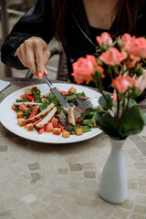 Woman enjoying a fresh salad at a restaurant, with flowers in the foreground.