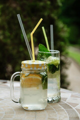 Refreshing summer drinks with straws and citrus fruits on a mosaic table outdoors.