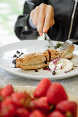Person cutting into a delicious dessert with fresh berries and cream.