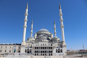 Frontal view of Kocatepe Mosque with central dome, tall minarets, marble facade and steps;...