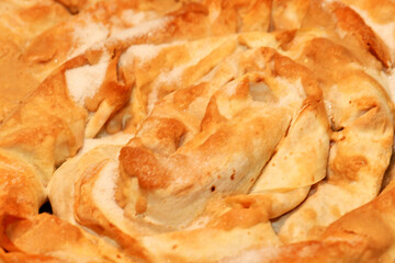 A close-up of a freshly baked, spiral tahinli pita, a traditional Cypriot tahini pie. The flaky, golden pastry is a delicious and authentic dish, perfect for a treat.