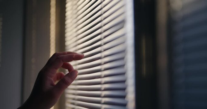 Woman look over the window with blinds at sunset. The blinds are open, allowing sunlight to shine through. The room appears to be well-lit and bright, creating a warm and inviting atmosphere