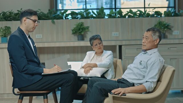 Male psychologist talking to a senior couple during therapy session in modern office, providing emotional support and professional counseling for mental health, communication and relationship care