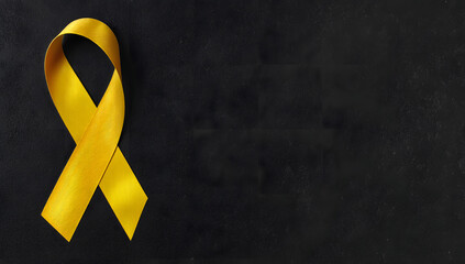 Yellow ribbon on black background, symbolizing cancer awareness and support with copy space for health campaigns and title banners
