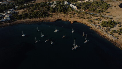 Drone view of multiple sailboats anchored in a calm bay of Ibiza