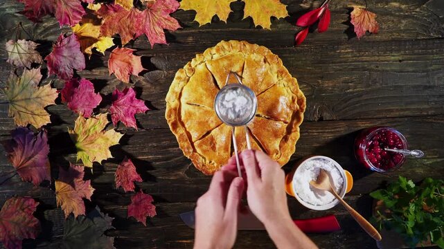 Hands topping an autumn apple pie with a sieve Thanksgiving celebration.