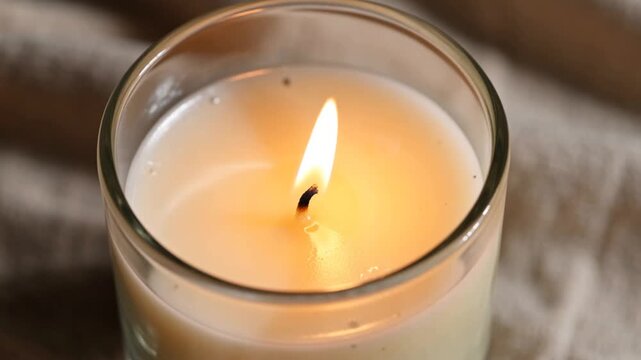 Close-up of a lit candle in a glass jar with a warm glow