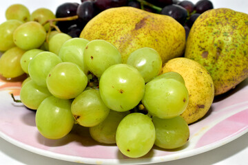 On a ceramic dish lie ripe and juicy fruits such as grapes and pears.