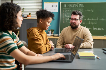 Caucasian man teaching multiethnic teenagers using laptops in classroom, students listening and engaging in discussion, chalkboard with AI prompting instructions visible in background