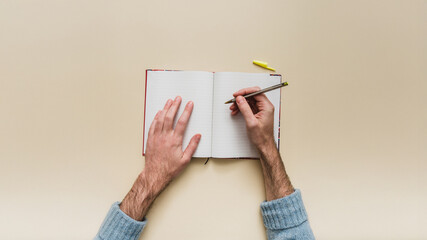 A blank notebook on a neutral background with hands in a writing position. A symbol of planning,...