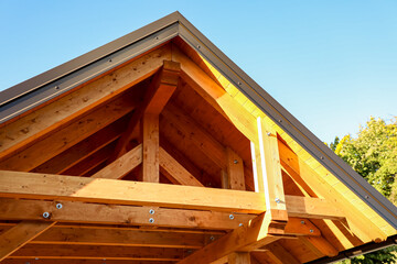 Obraz premium Sunlight gently filters through a beautifully constructed wooden roof framework, revealing exposed beams and strong bolts that emphasize the rich grain of natural wood.