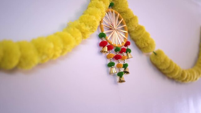  Traditional Indian marigold garland (genda phool) with a colorful bell ornament, hanging on a white wall for Diwali or a wedding
