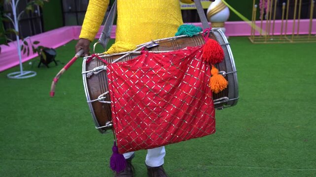 Close-up of Indian musician in yellow kurta holding a decorated Dhol drum with tassels, ready for festive performance.