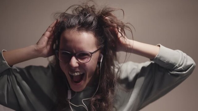 Excited woman with long curly hair and glasses dancing crazy laughing and yelling into her earbuds, enjoying herself on favour music