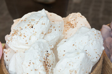 A close-up of large white meringues sprinkled with crushed nuts displayed in a basket.