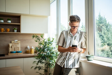 Young man browsing mobile phone in modern kitchen