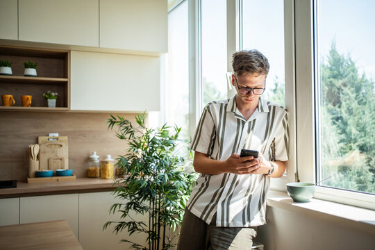 Young man browsing mobile phone in modern kitchen