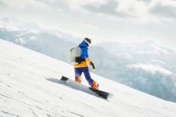 Snowboarder riding downhill on snowy slope with backpack and mountains in background on winter day
