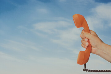 Orange retro telephone handset held against blue sky