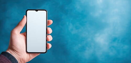 Hand holding smartphone with blank screen against blue background.