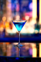 Blue cocktail glass on reflective bar table with moody lights
