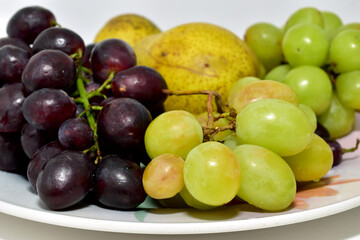 On a ceramic dish lie ripe and juicy fruits such as grapes and pears.