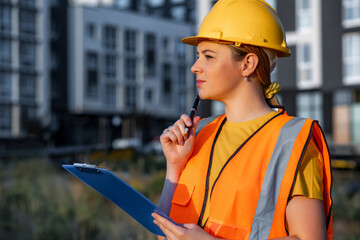 Confident female construction worker analyzing a project site with a clipboard in hand