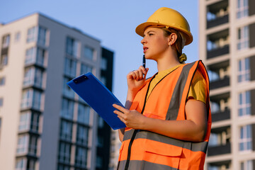 Female construction worker with clipboard near modern buildings outdoors