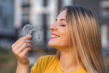 Smiling woman holding clear aligners outdoor with blurred background