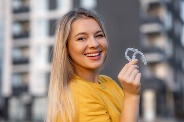 Smiling woman outdoors holding clear aligners for teeth care and orthodontic health