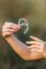 Hands carefully holding a pair of transparent dental aligners outdoors