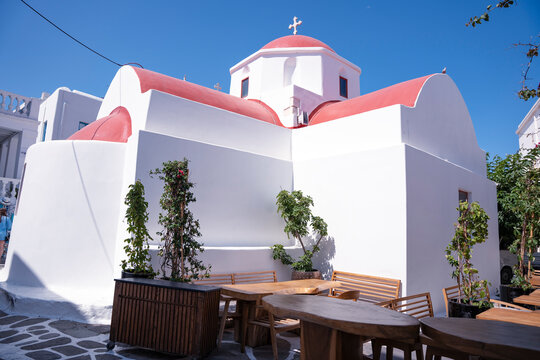 White Greek church with red door seen through narrow alley on a sunny day - Powered by Adobe