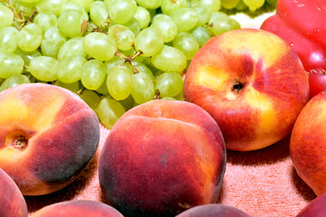 Ripe and juicy fruits such as green and blue grapes, peaches and persimmons lie on the table.